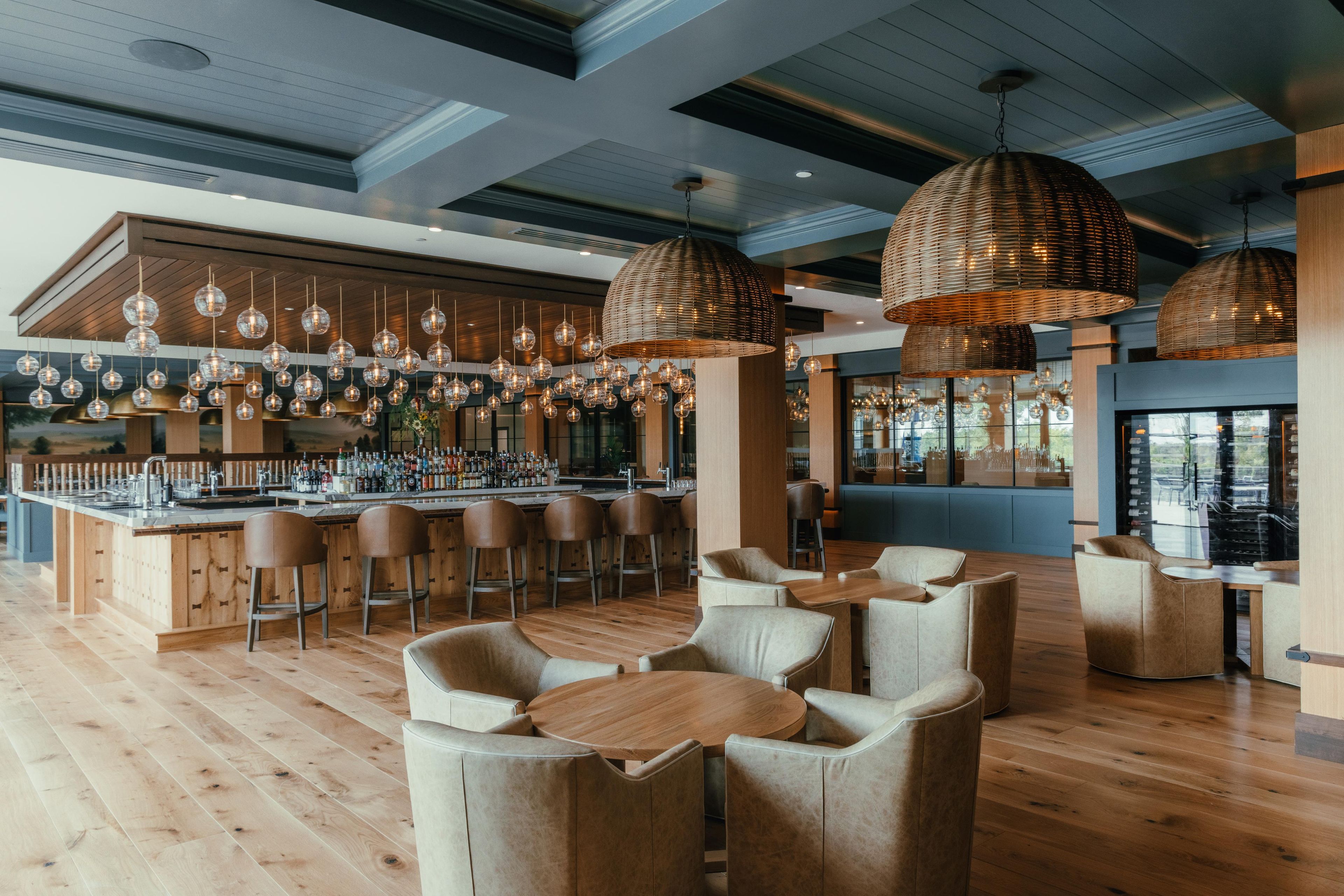 A bar area with wooden bar counters, multiple hanging light fixtures, and seating with round tables and chairs.