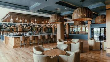 A modern bar area with wooden flooring, multiple hanging pendant lights, bar stools, and a bar counter with a variety of bottles.