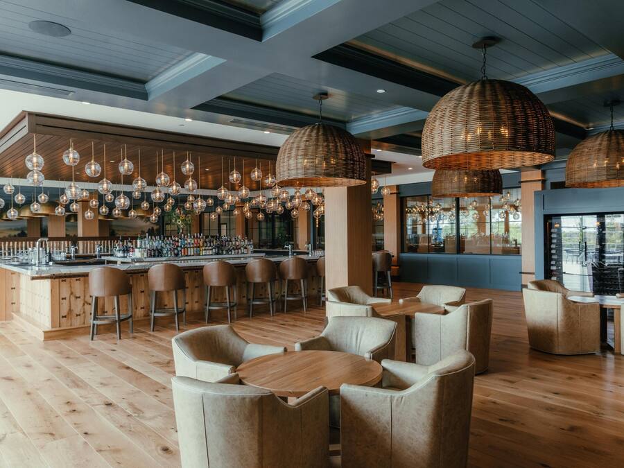 A modern bar area with wooden flooring, multiple hanging pendant lights, bar stools, and a bar counter with a variety of bottles.