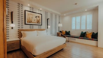 A bedroom with a wooden bed, a wall-mounted picture, a bedside table, a bench with cushions, and a window with blinds.