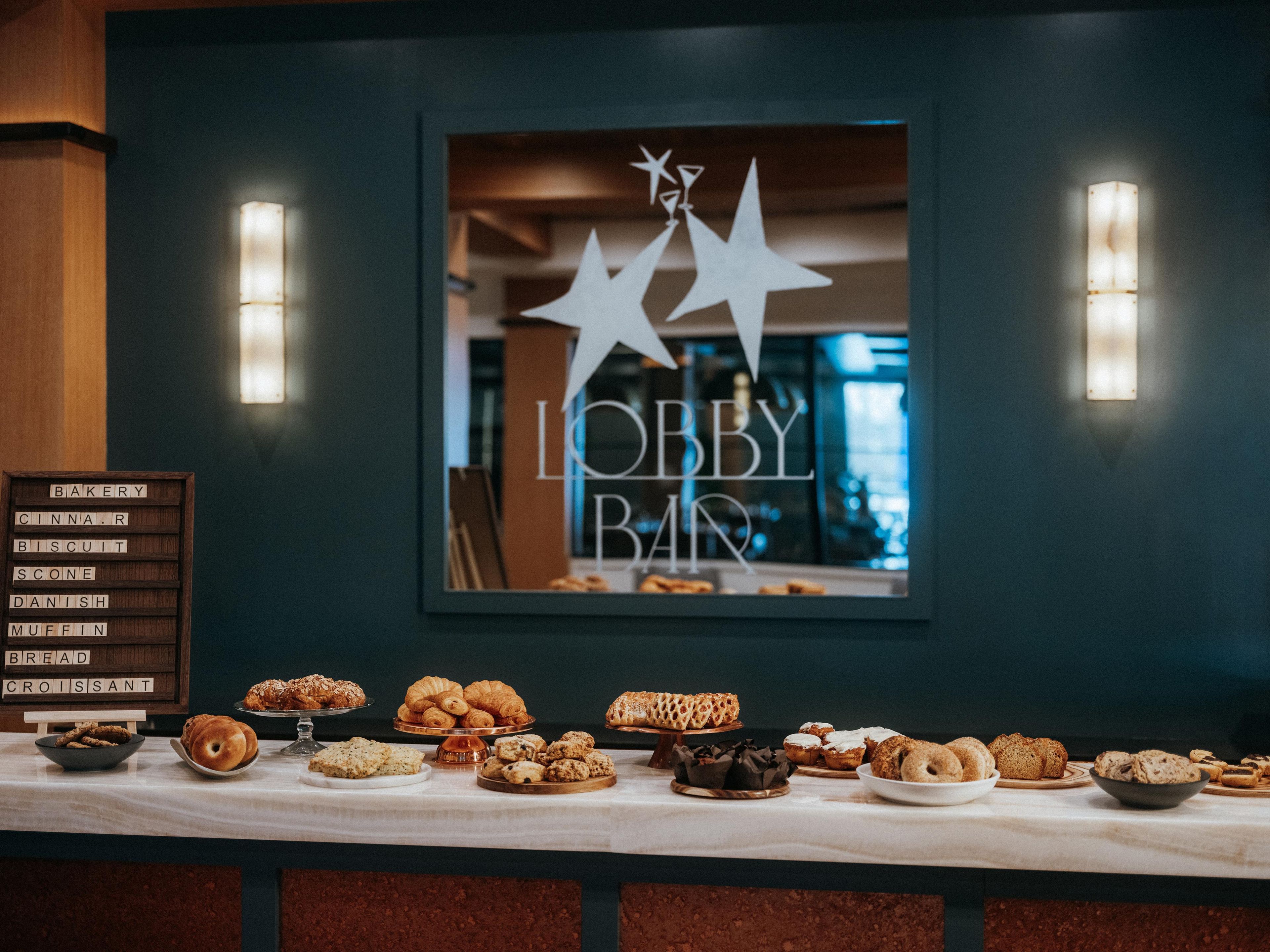 Mesa de buffet com diversos produtos de panificação e um aviso que diz 'LOBBY BAN'.