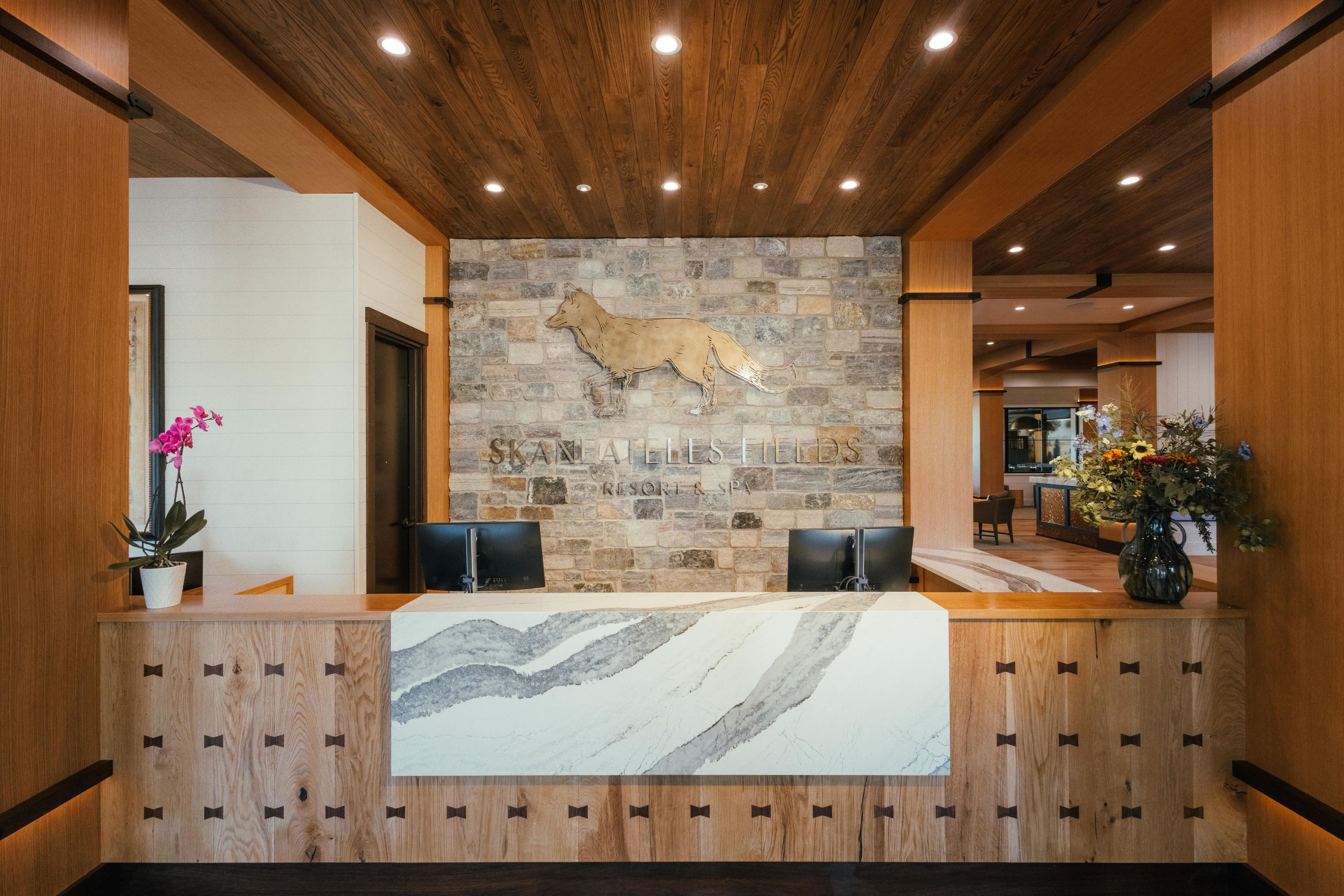 Un comptoir d’accueil avec un mur en pierre en arrière-plan, un espace d’accueil en bois et un comptoir d’accueil au design évoquant le marbre.