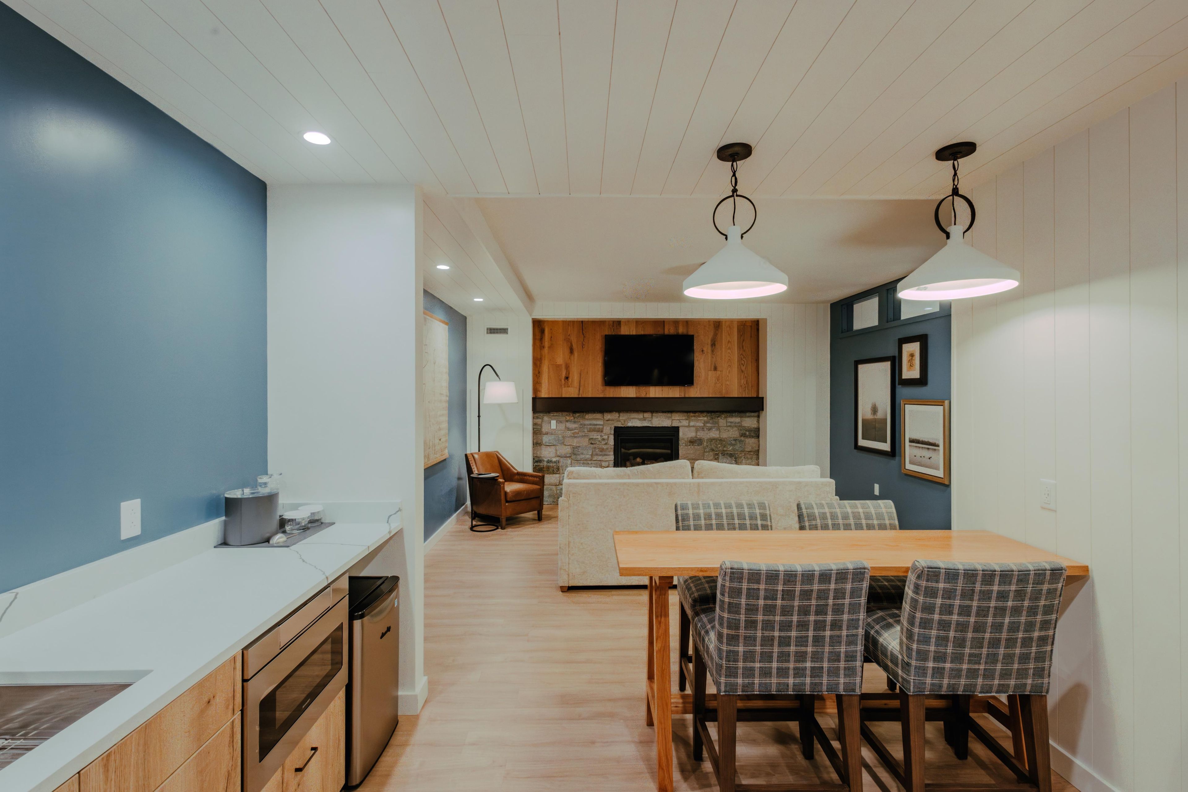 A modern kitchen with a wooden countertop, a dining area with plaid chairs, and a fireplace.