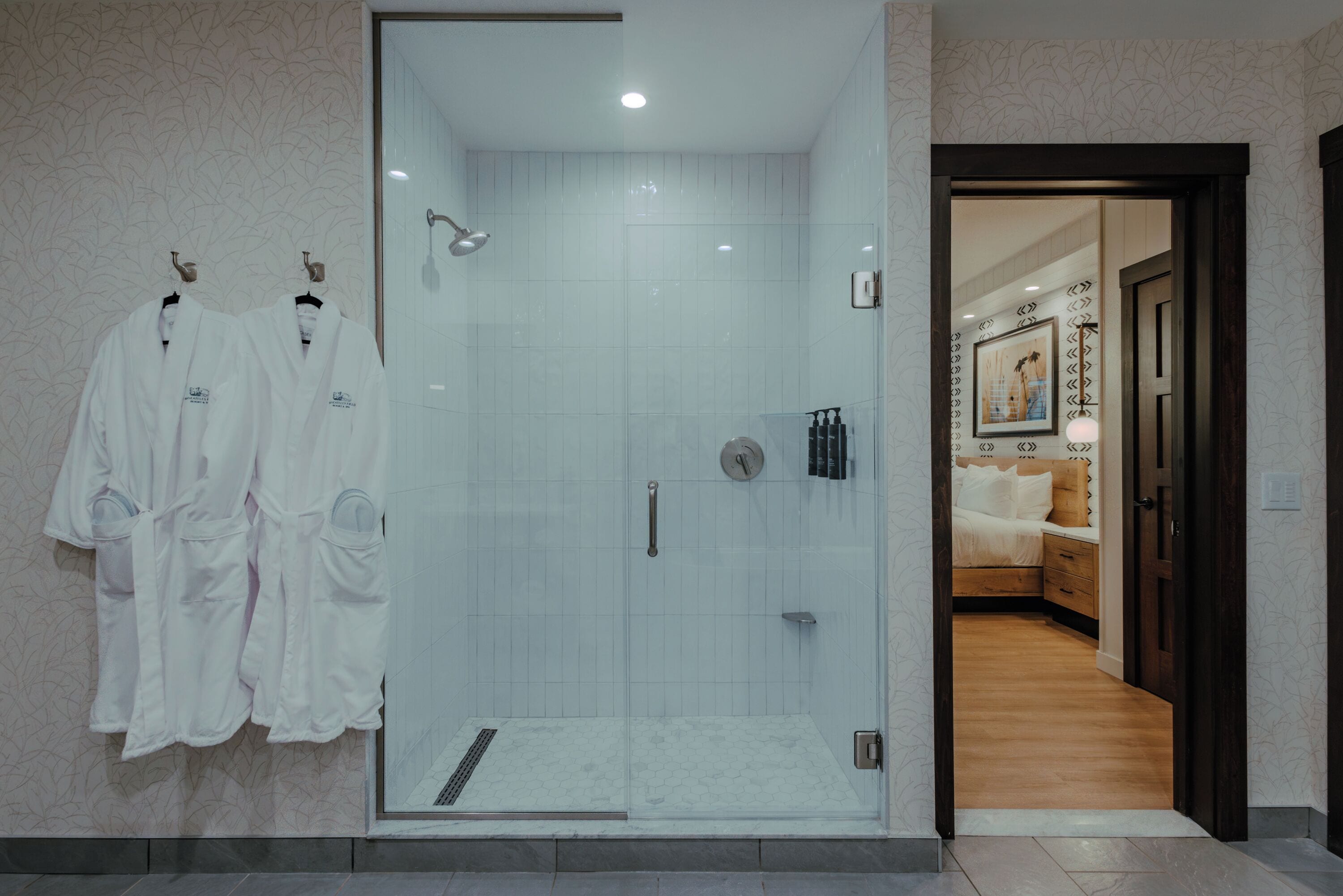 Un espace douche fermé par des parois de verre, avec un mur carrelé, une pomme de douche visible et une barre d’appui.