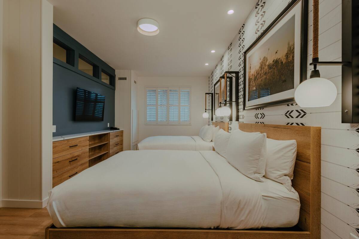 Un dormitorio con dos camas, televisor y una ventana grande.