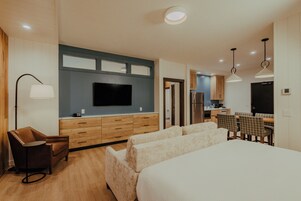 Una habitación de hotel moderna con televisor de pantalla plana, sofá, mesa de comedor con sillas y kitchenette.