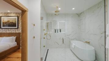 A modern bathroom with a glass-enclosed shower, a freestanding bathtub, and a wooden bed with white bedding.
