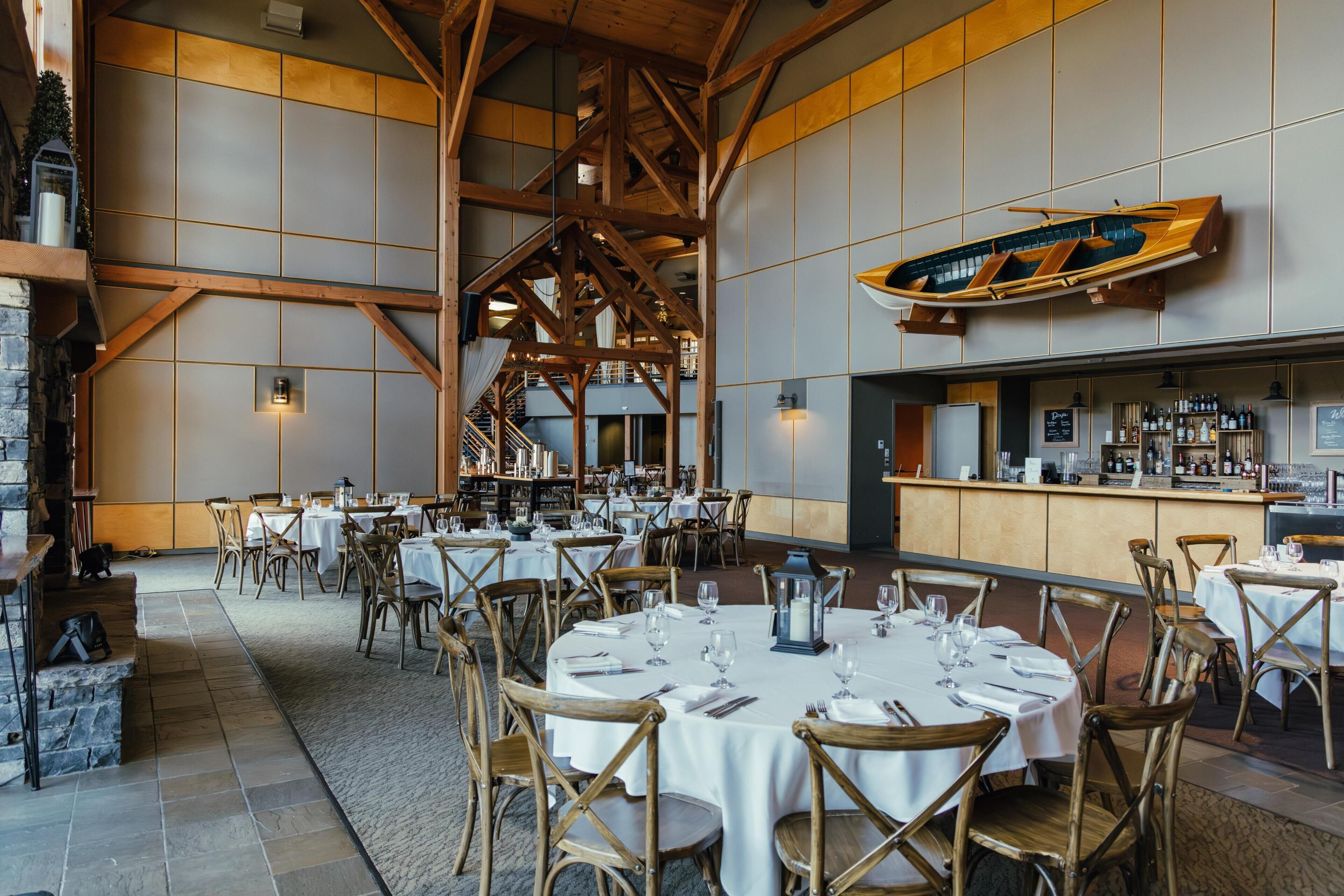 A restaurant with round tables, wooden chairs, a bar area, and a large wooden boat decoration.
