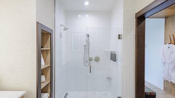 A modern bathroom with a shower, a wooden shelf with towels, and a white tiled floor.