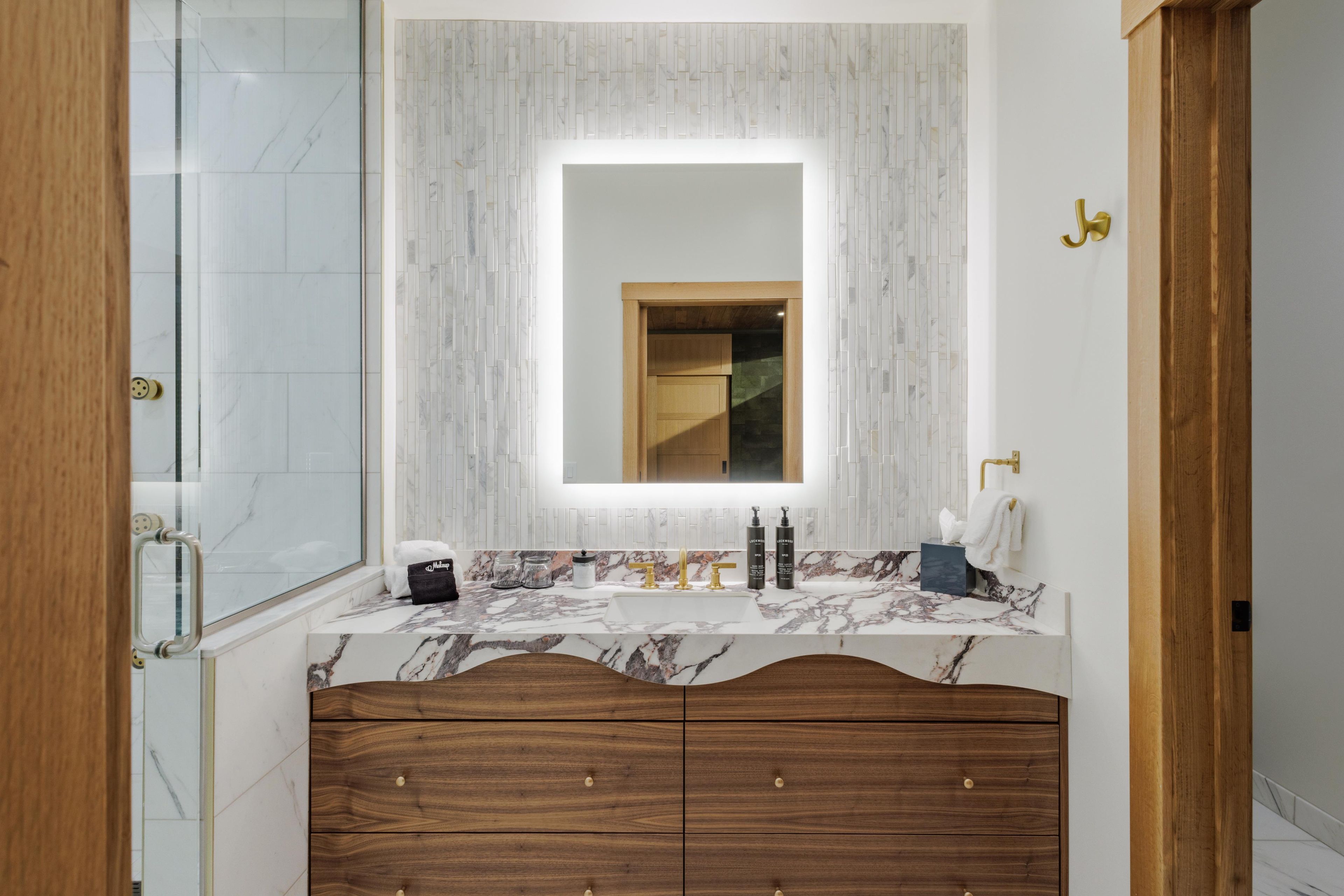 Un baño moderno con tocador de mármol, un espejo grande y un armario de madera.