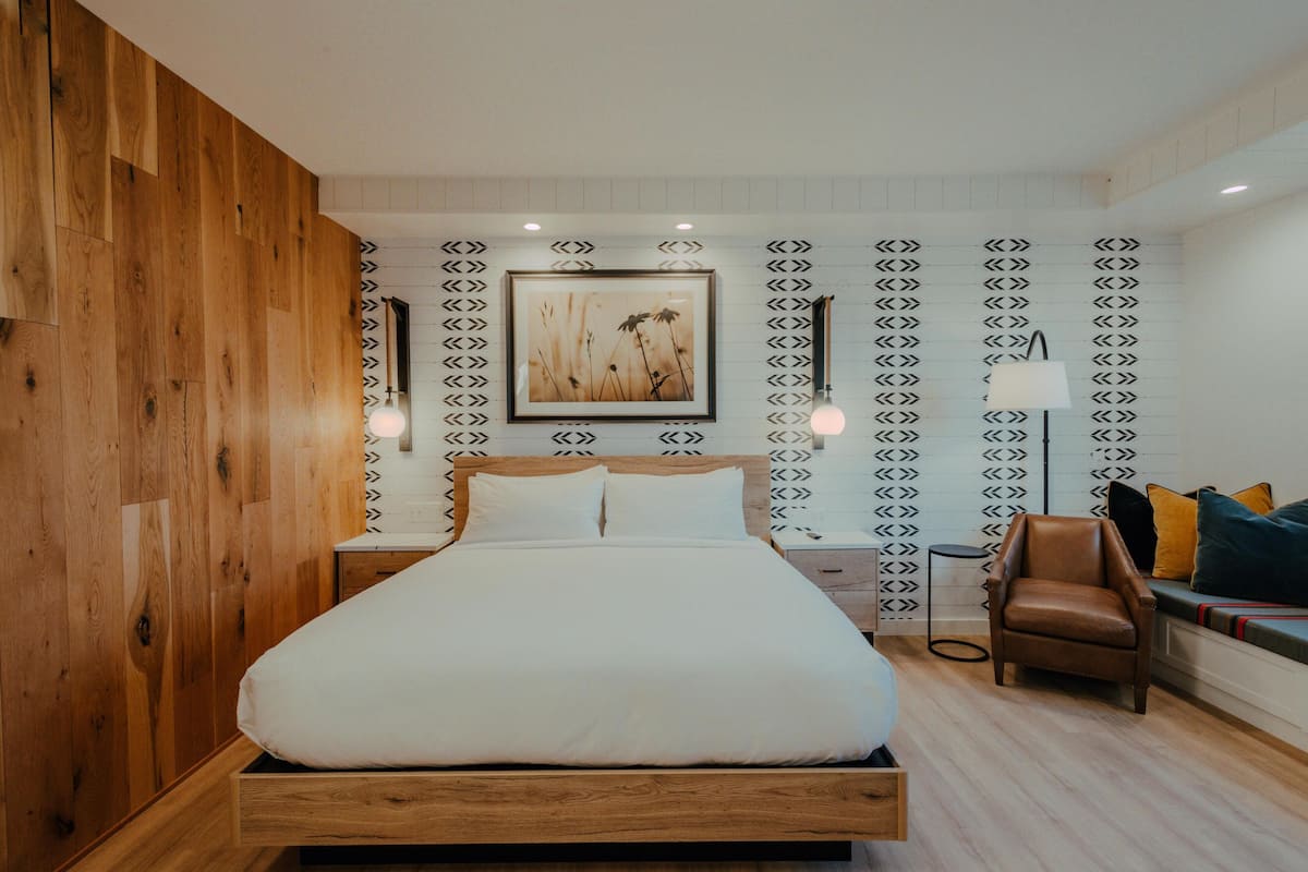 A bedroom with a wooden bed, a nightstand, a chair, and a wall-mounted lamp.