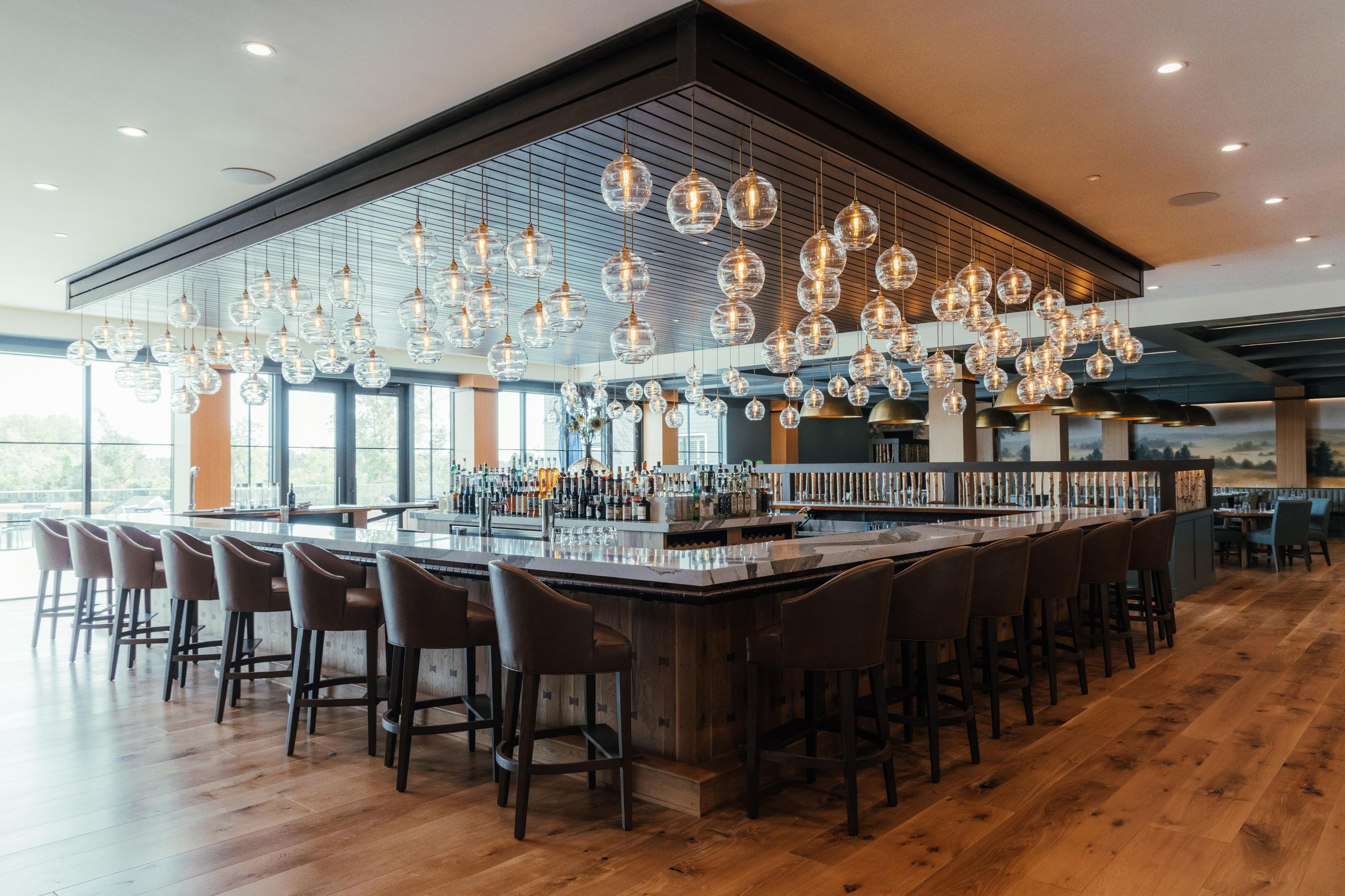 A bar area with a long counter, multiple stools, and hanging spherical light fixtures.