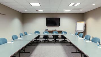 Une salle de conférence équipée d’une longue table, de chaises, d’un téléviseur à écran plat, d’un tableau blanc et d’un projecteur.