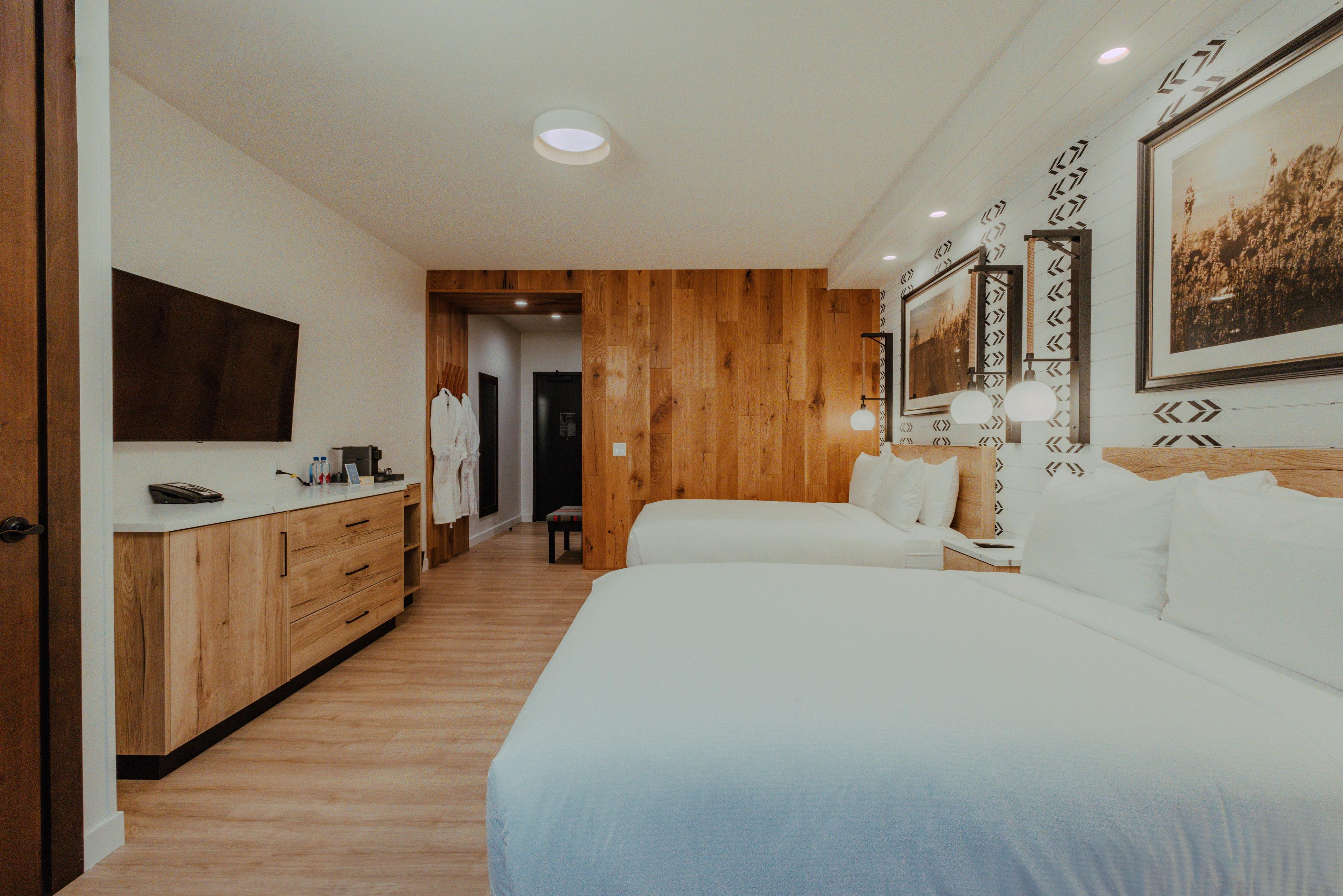 Une chambre d’hôtel avec un plancher en bois, un lit, un bureau avec un téléphone et un téléviseur fixé au mur.