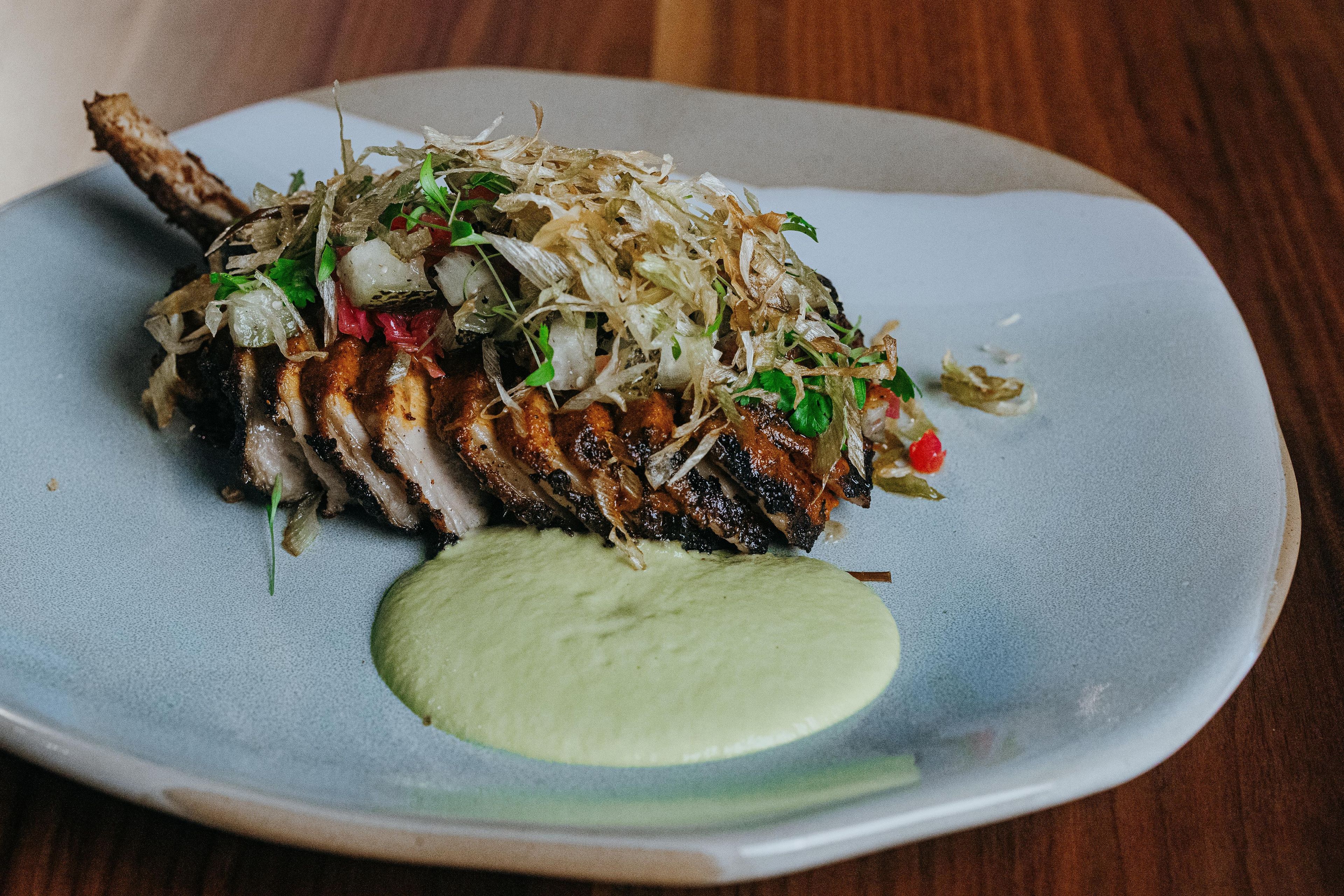 A plate of food with a piece of meat, vegetables, and a green sauce.