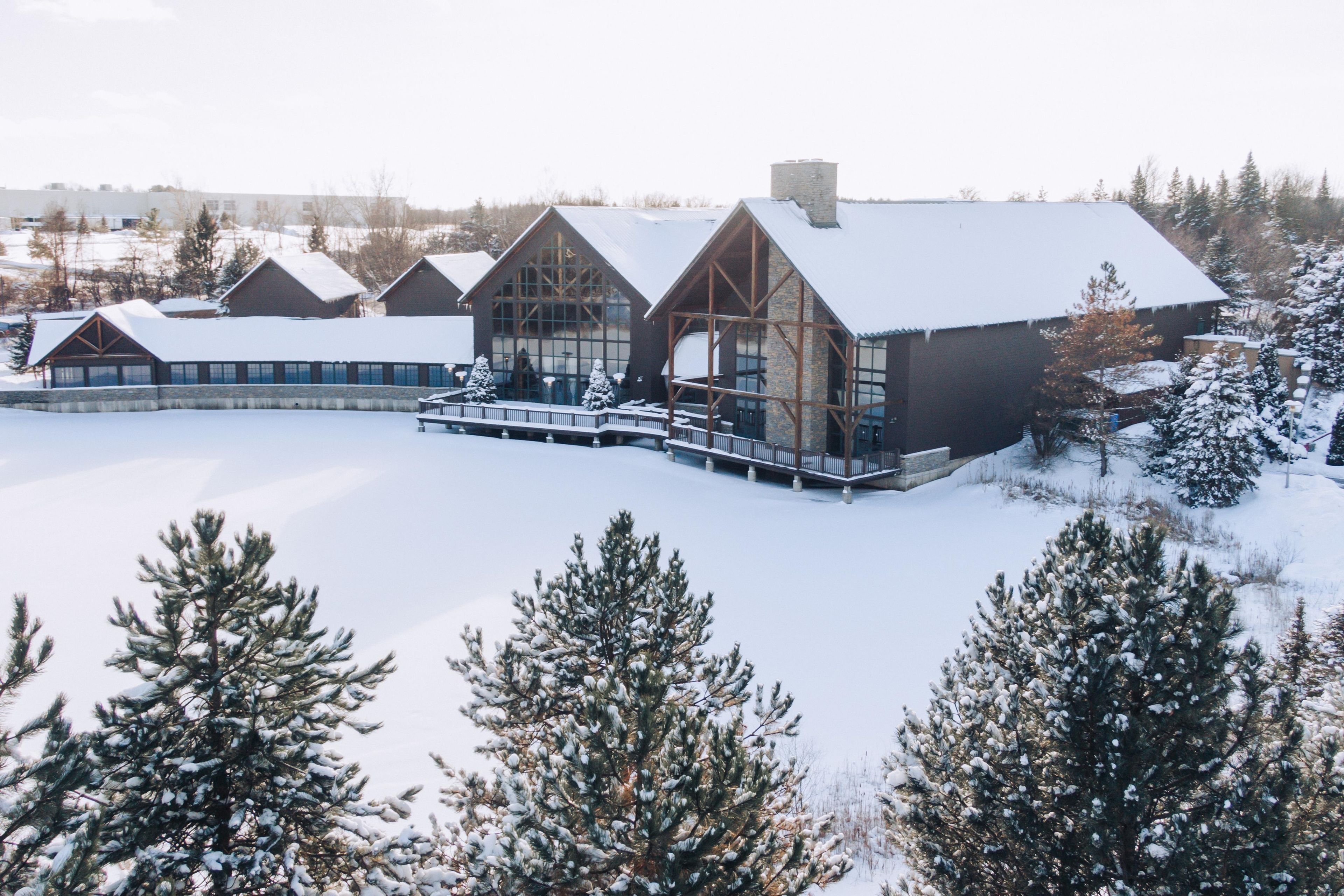 A large lodge with multiple cabins, a covered walkway, and snow-covered trees.