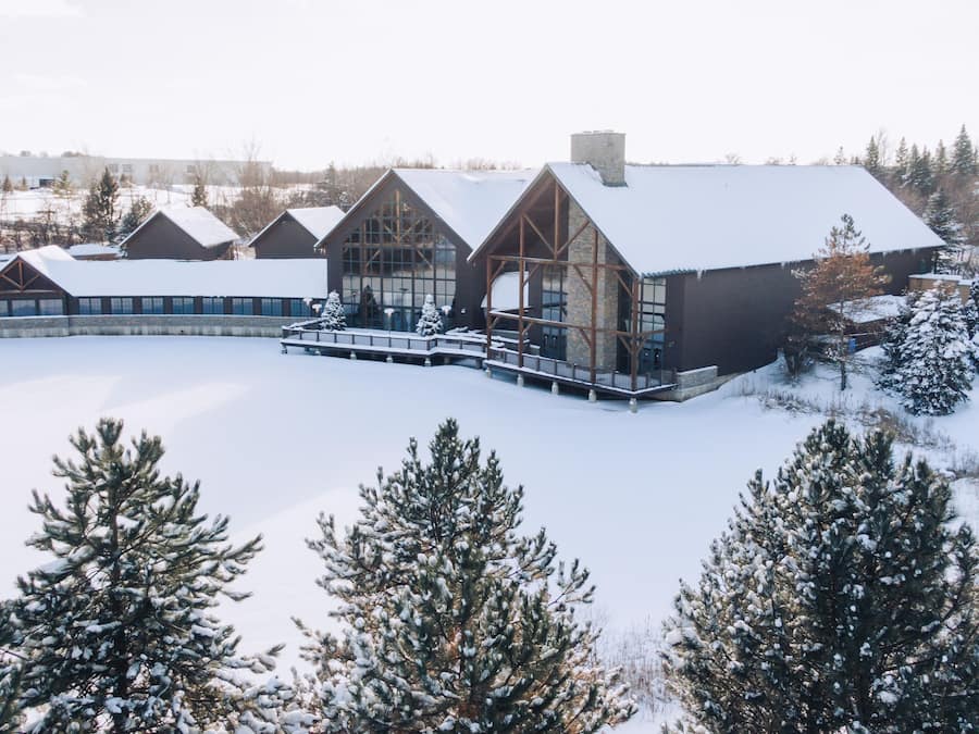 Un grand chalet doté de plusieurs cabanes, d’une allée couverte et d’arbres couverts de neige.
