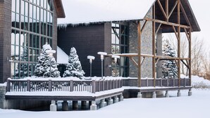 A modern building with large windows, a wooden deck, and snow-covered surroundings. - Skaneateles Fields Resort & Spa, Curio Collection By Hilton (Skaneateles)