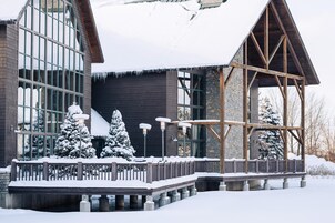 A modern building with large windows, a wooden deck, and snow-covered surroundings.
