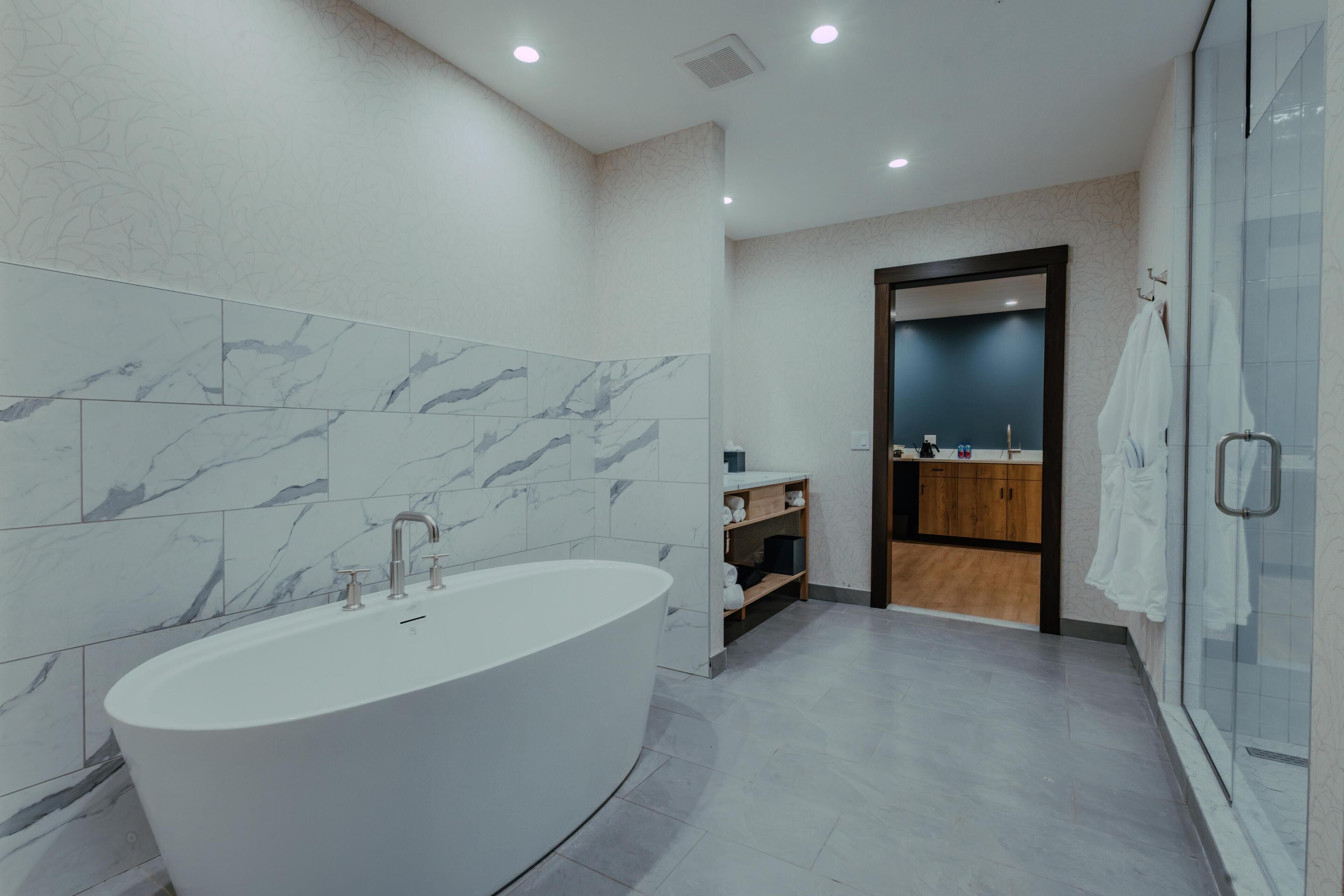 A modern bathroom with a freestanding bathtub, a glass shower enclosure, and a wooden vanity with a mirror.