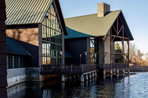 A waterfront building with large windows, a metal roof, and a wooden deck extending over water. - Skaneateles Fields Resort & Spa, Curio Collection By Hilton (Skaneateles)