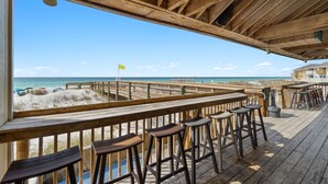 A wooden deck with bar stools overlooking a beach with a flag.