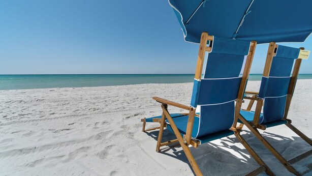 A beach chair and umbrella setup on a sandy beach with a clear blue sky.