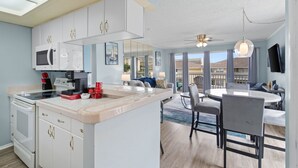 A modern kitchen with white cabinets, a microwave, and a coffee maker. There is a dining area with a round table and chairs.
