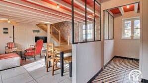 A spacious living area with a wooden dining table and chairs, a staircase, and a view of the outside through a window.