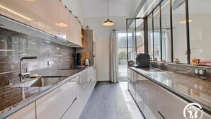 A modern kitchen with a sleek design, featuring a stainless steel sink, a marble countertop, and pendant lighting.