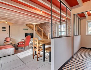 A spacious living area with a wooden dining table and chairs, a staircase, and a view of the outside through a window. - Le Pressoir - GUIDEL (GUIDEL)