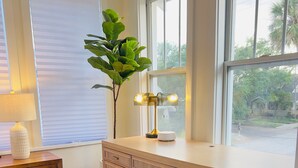 Une chambre avec un bureau en bois, une lampe de chevet, une plante en pot et une vue sur l’extérieur.