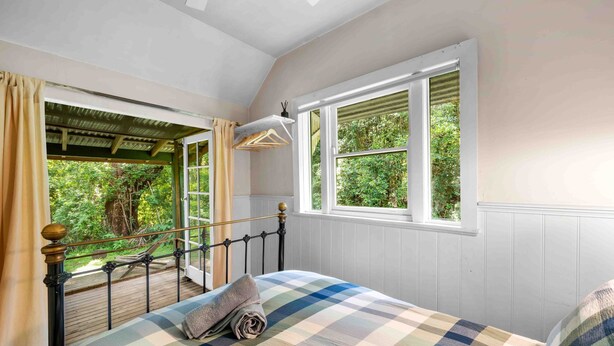 Un dormitorio con cama, ventana con vista a la vegetación y balcón con barandilla.