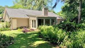 A single-story house with a covered porch, surrounded by lush greenery and a well-maintained lawn.