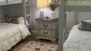 Ein Schlafzimmer mit Etagenbetten, einer Kommode mit Schubladen, einem Spiegel, einer Lampe und einem floralen Teppich.