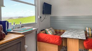 A compact RV interior with a window offering a view of a green field, a sink with a faucet, a television mounted on the wall, and a small table with a marble top. - 1 bedroom accommodation in Ormskirk (Ormskirk)