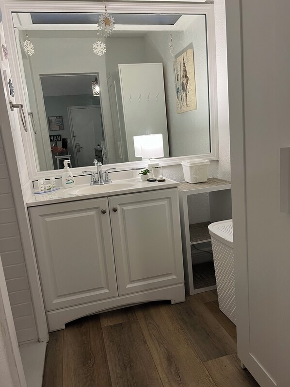 A bathroom with a white vanity, a large mirror, and a sink with toiletries.