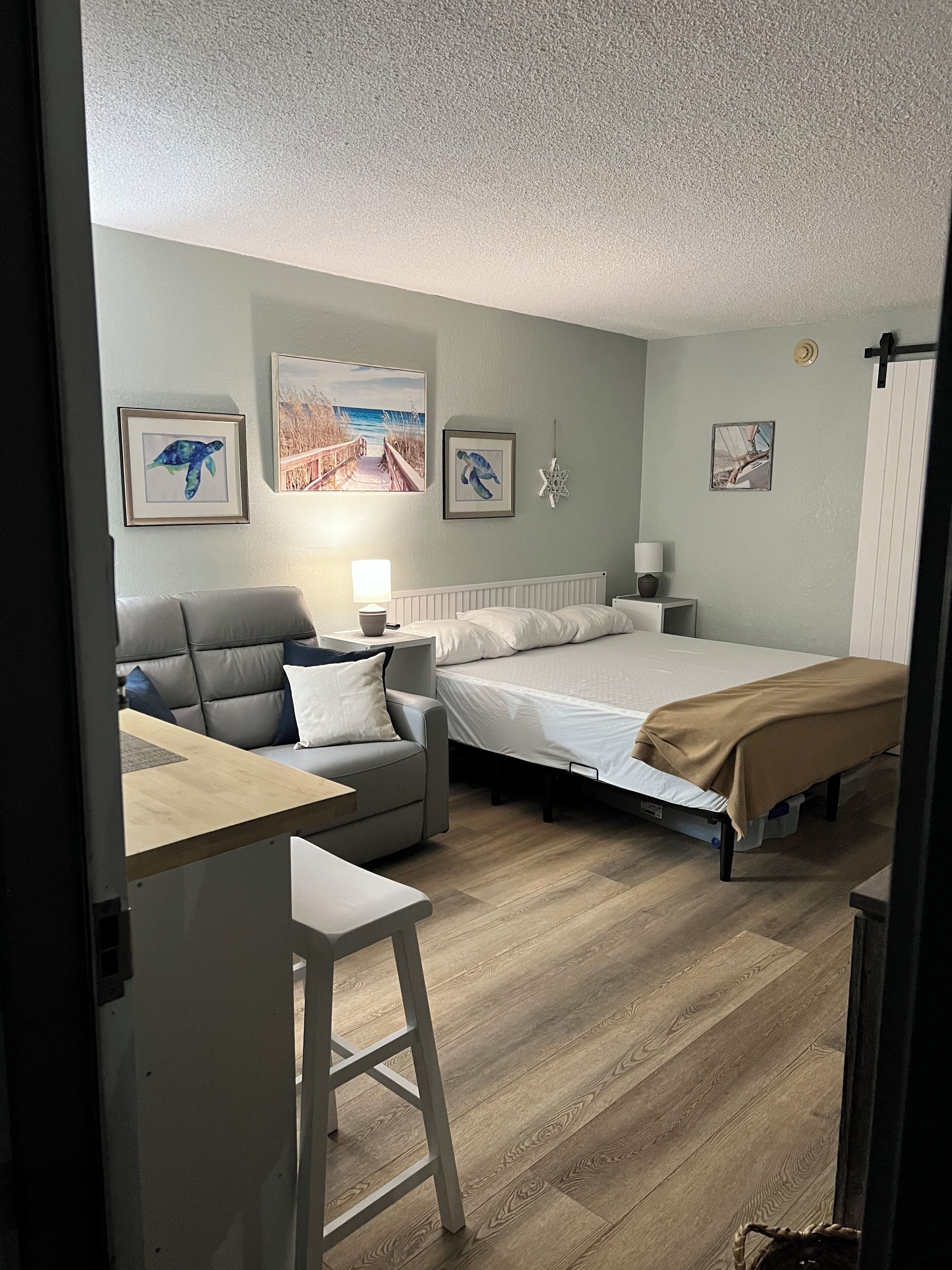 Ein Schlafzimmer mit Bett, einer Couch, einem Schreibtisch und einem Sessel. An den Wänden befinden sich Bilder und eine Meerstern-Dekoration.