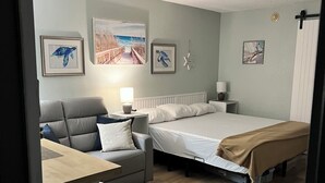 A bedroom with a bed, a sofa, a desk, and a chair. There are wall-mounted pictures and a starfish decoration. - Cozy condotel with King Bed, WiFi, great pool, fitness room and much more! (Sarasota)