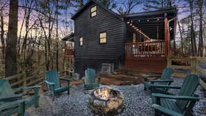 A cabin with a deck, outdoor seating, and a fire pit.