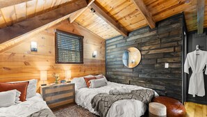 A cozy bedroom with two beds, wooden walls, a large window, and a round mirror.