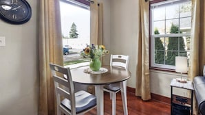 A dining area with a round table, white chairs, a vase with flowers, and a clock on the wall. - Charming Bungalow 1 Duplex in Lebanon. (Lebanon)