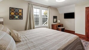 A bedroom with a large bed, a window with curtains, a flat-screen TV, a wooden dresser, and a framed artwork on the wall. - Charming Bungalow 1 Duplex in Lebanon. (Lebanon)