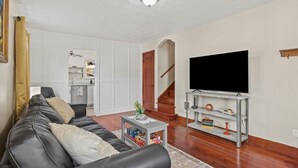 A living room with a black leather sofa, a flat-screen TV on a wooden stand, a small table with decorative items, and a staircase leading to an upper floor. - Charming Bungalow 1 Duplex in Lebanon. (Lebanon)