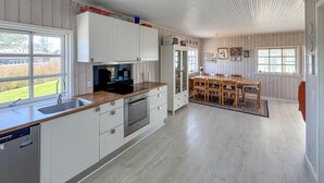 A modern kitchen with white cabinetry, a wooden countertop, and a dining area with a table and chairs. - Cozy home in Juelsminde with WiFi (Juelsminde)