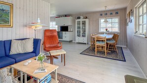 A living room with a blue sofa, a red chair, a dining table with chairs, a kitchen area, and a window with a view. - Cozy home in Juelsminde with WiFi (Juelsminde)