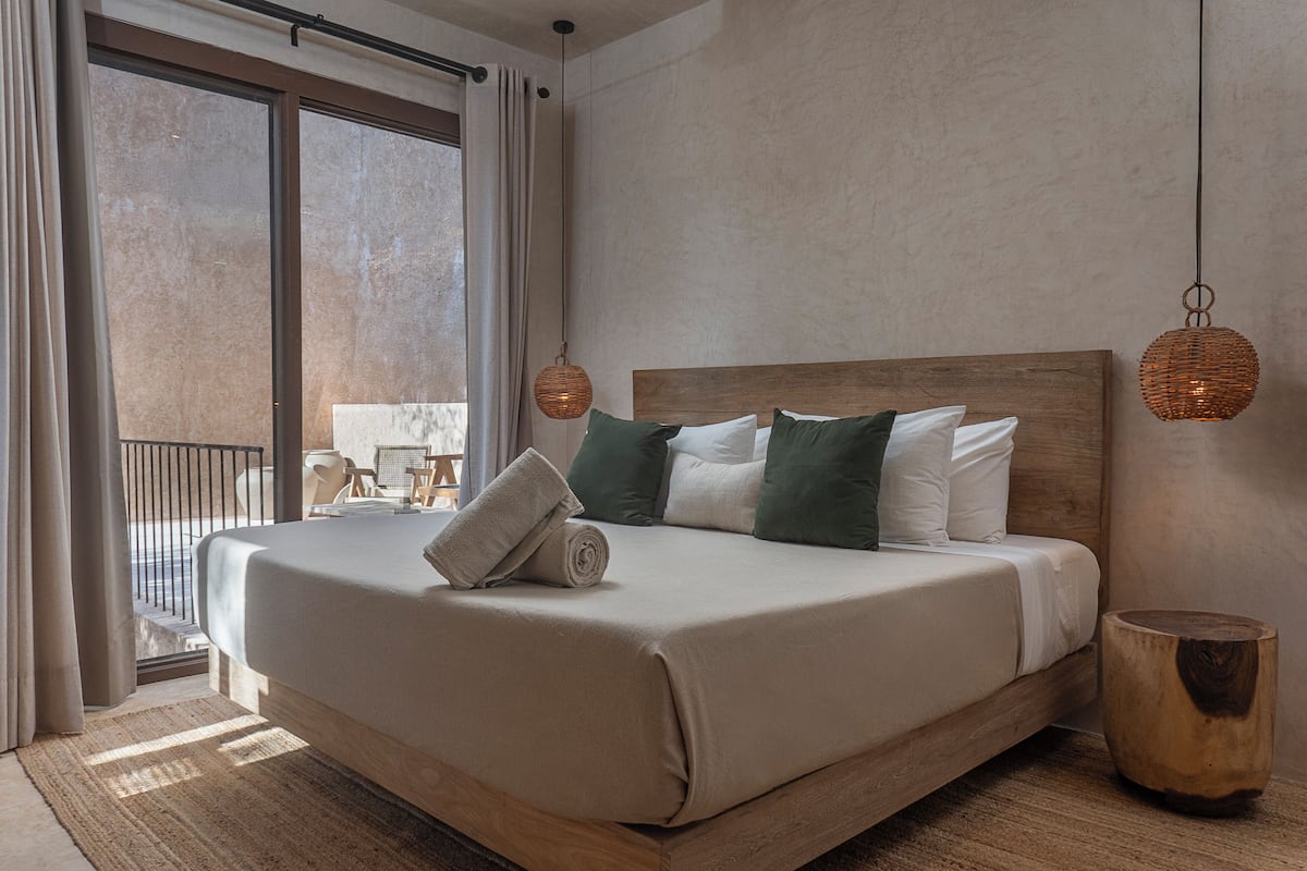 A neatly made bed with a wooden headboard, a rolled towel, and green and white pillows.