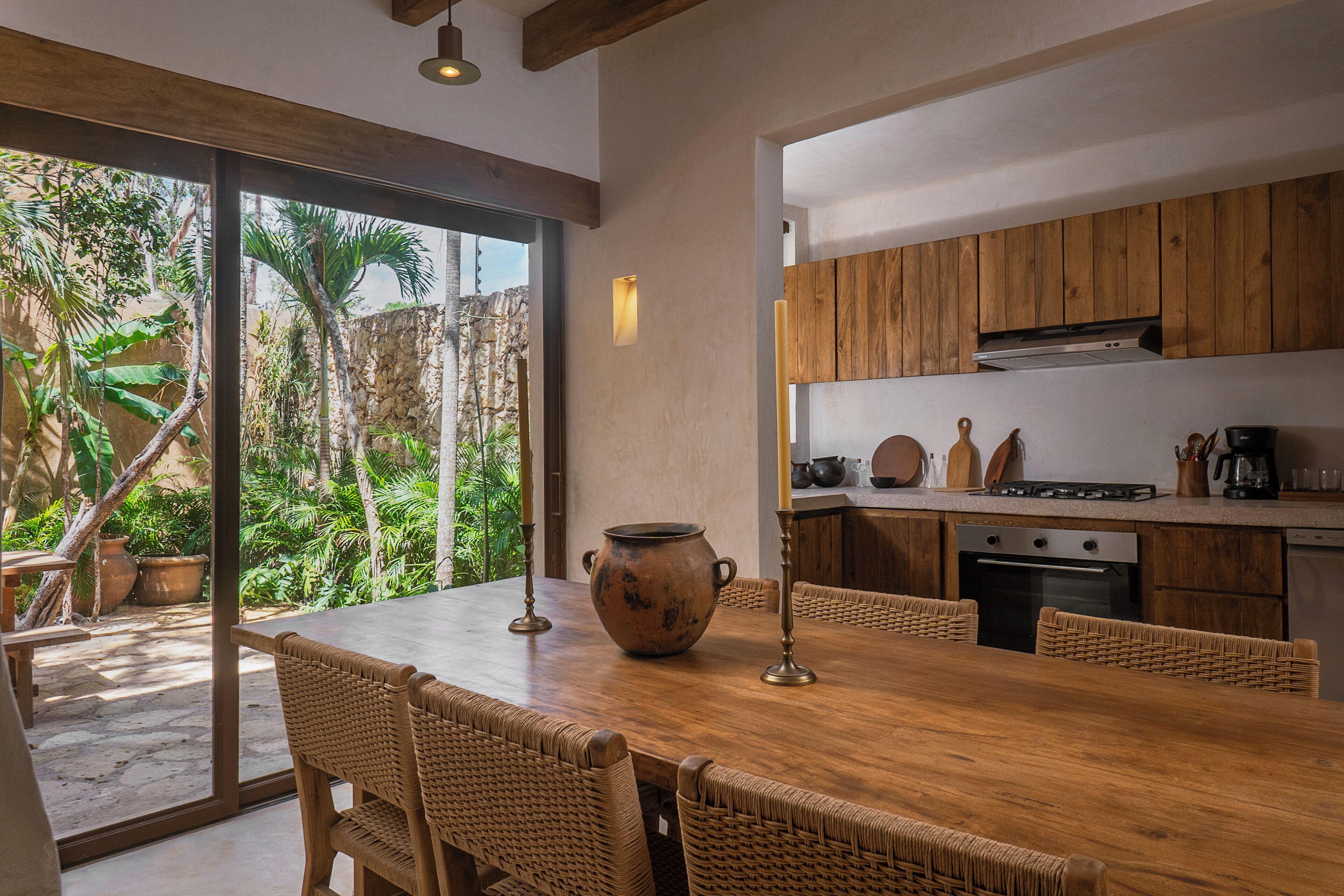A modern kitchen with wooden cabinets, a large dining table, and a view of a lush garden.