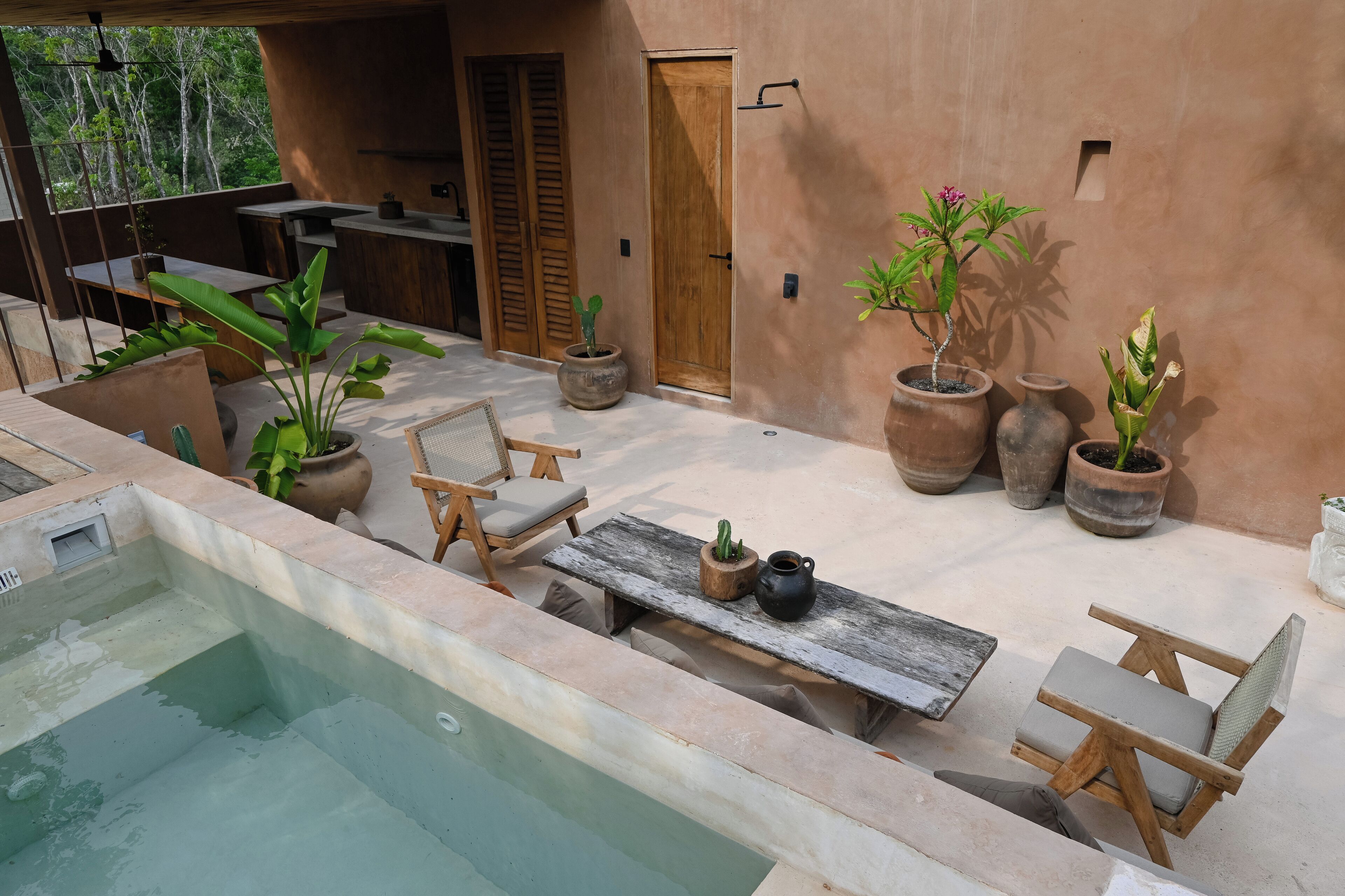 A poolside area with a wooden table, chairs, and potted plants.