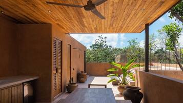 An outdoor patio with a wooden ceiling, a dining table, potted plants, and a view of the surrounding greenery.